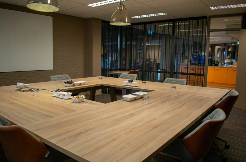 Vergaderruimte aan de Zaagmolenlaan met een grote U-vormige houten tafel, comfortabele stoelen en moderne verlichting.