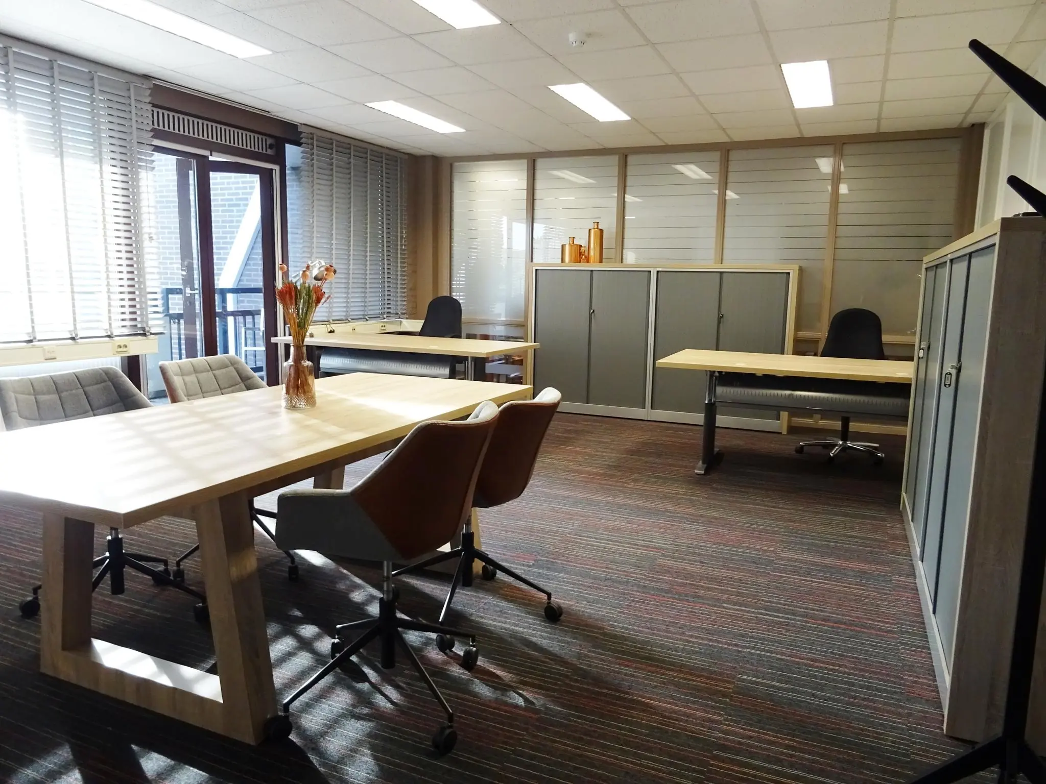 Moderne kantoorruimte aan de Zaagmolenlaan met bureaus, stoelen, kasten en grote ramen met jaloezieën.
