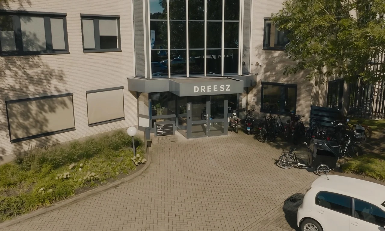 Vooraanzicht van het kantoorgebouw van Dreesz met fietsen en een auto voor de ingang.