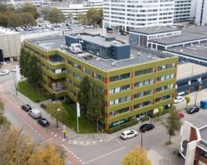 Luchtfoto van een groen kantoorgebouw aan de Treubstraat 1 in Rijswijk met omliggende wegen en geparkeerde auto’s.