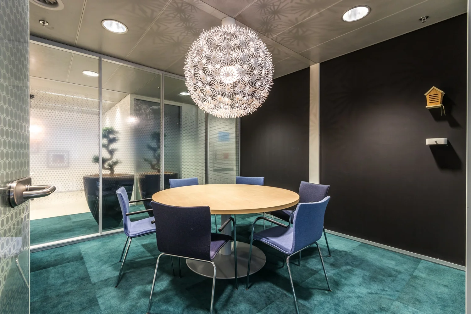Vergaderruimte aan de Reactorweg met ronde houten tafel, zes stoelen, opvallende bolvormige hanglamp en glazen wanden.