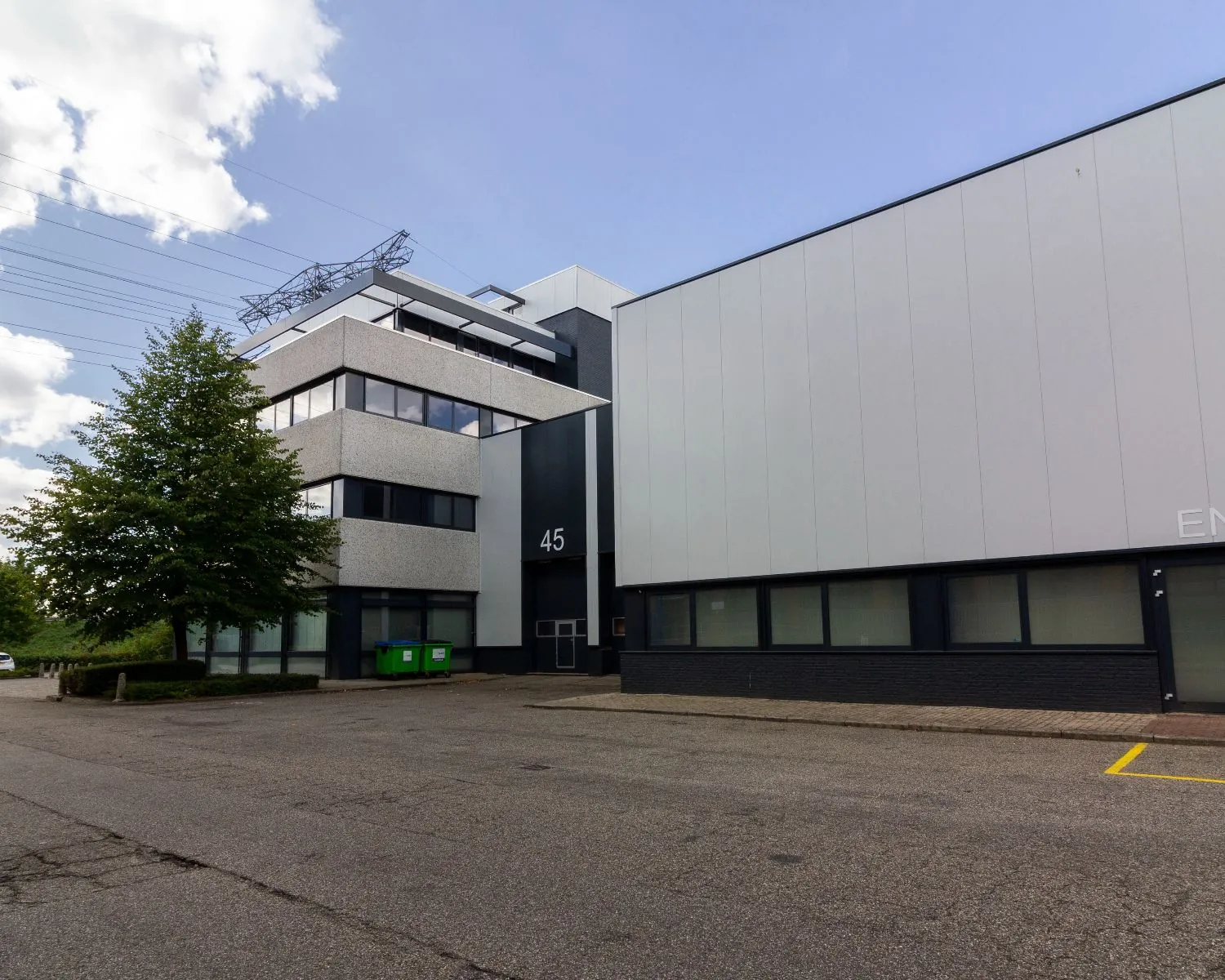 Kantoorgebouw met huisnummer 45 aan een rustige straat, met een boom en twee groene containers op de voorgrond.