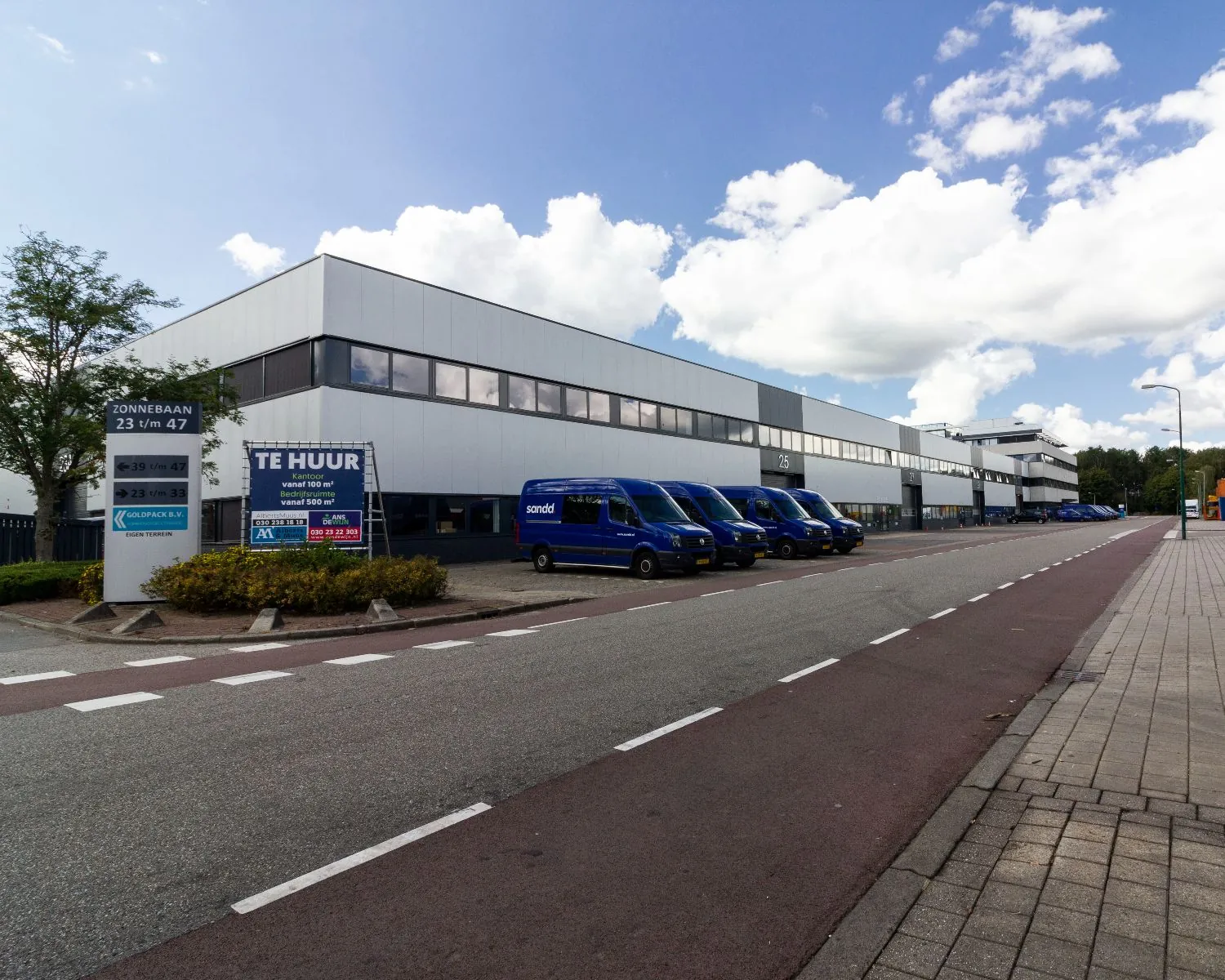 Bedrijventerrein aan de Zonnebaan met meerdere blauwe bestelbusjes en een gebouw met kantoorruimte te huur.
