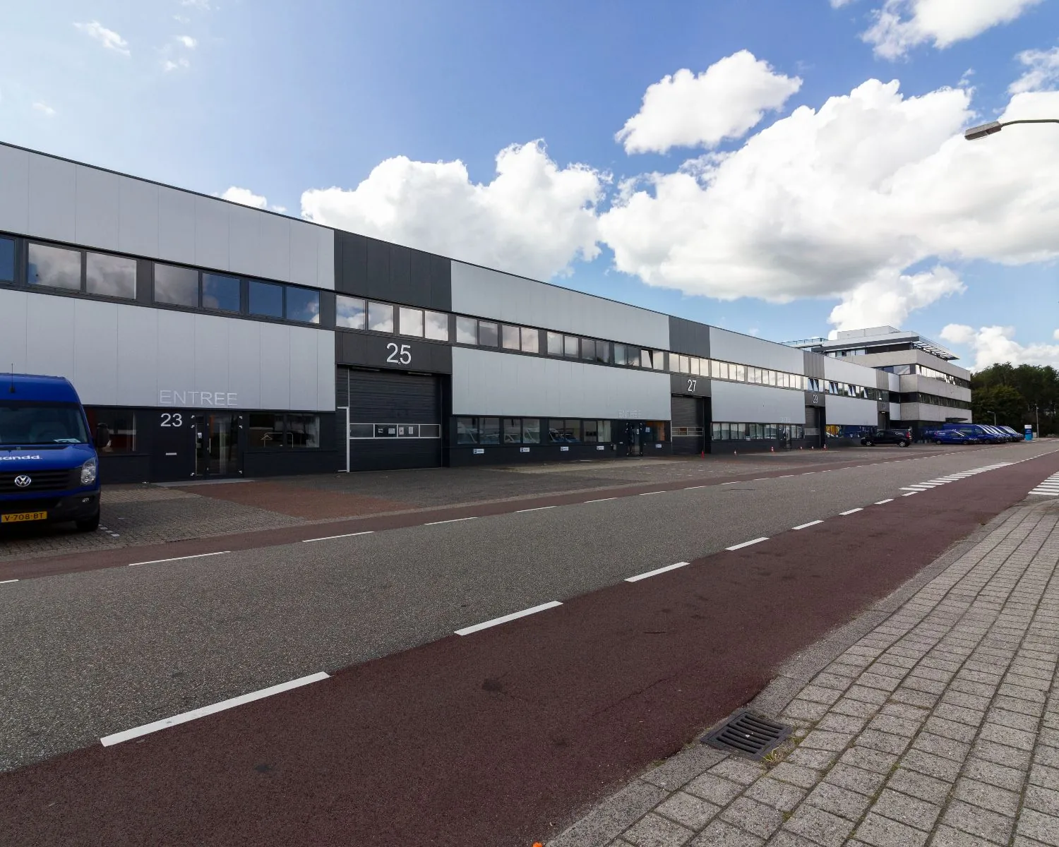 Langgerekt bedrijfsverzamelgebouw met de huisnummers 23 tot en met 31 aan een brede straat onder een deels bewolkte lucht.