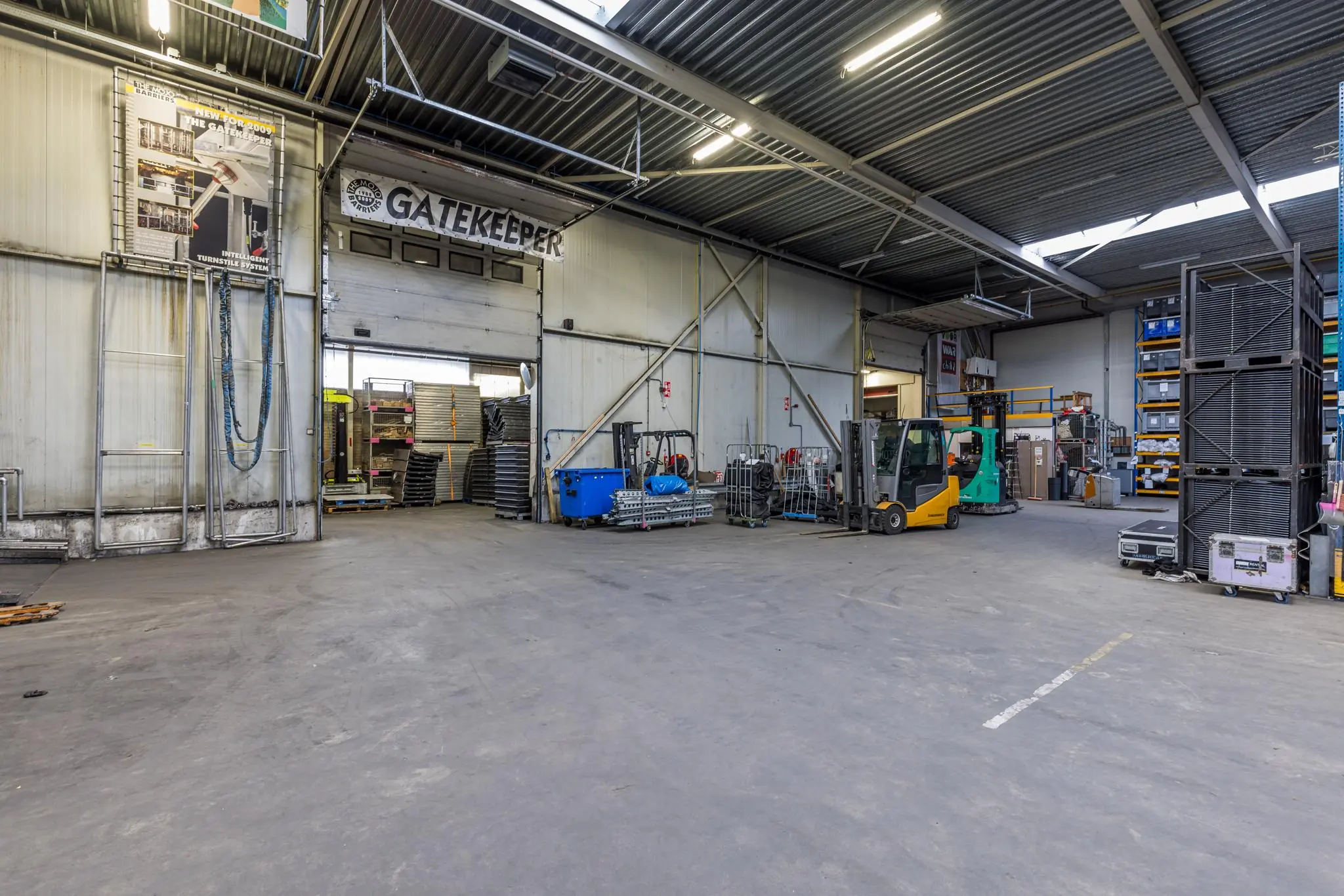 Magazijnruimte van Veldzigt met heftrucks, opslagrekken en materiaal bij de toegangspoort met het bord 'Gatekeeper'.