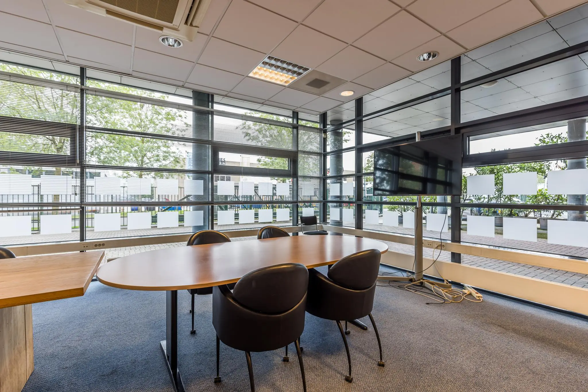 Vergaderruimte met ovale tafel, vier stoelen, grote ramen en een tv-scherm bij Veldzigt.