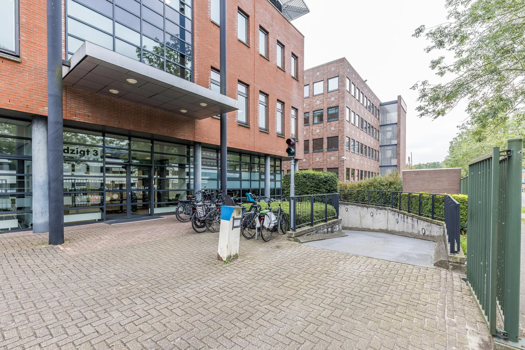 Ingang van kantoorpand Veldzigt 3 met fietsenstalling en oprit naar ondergrondse parkeergarage.