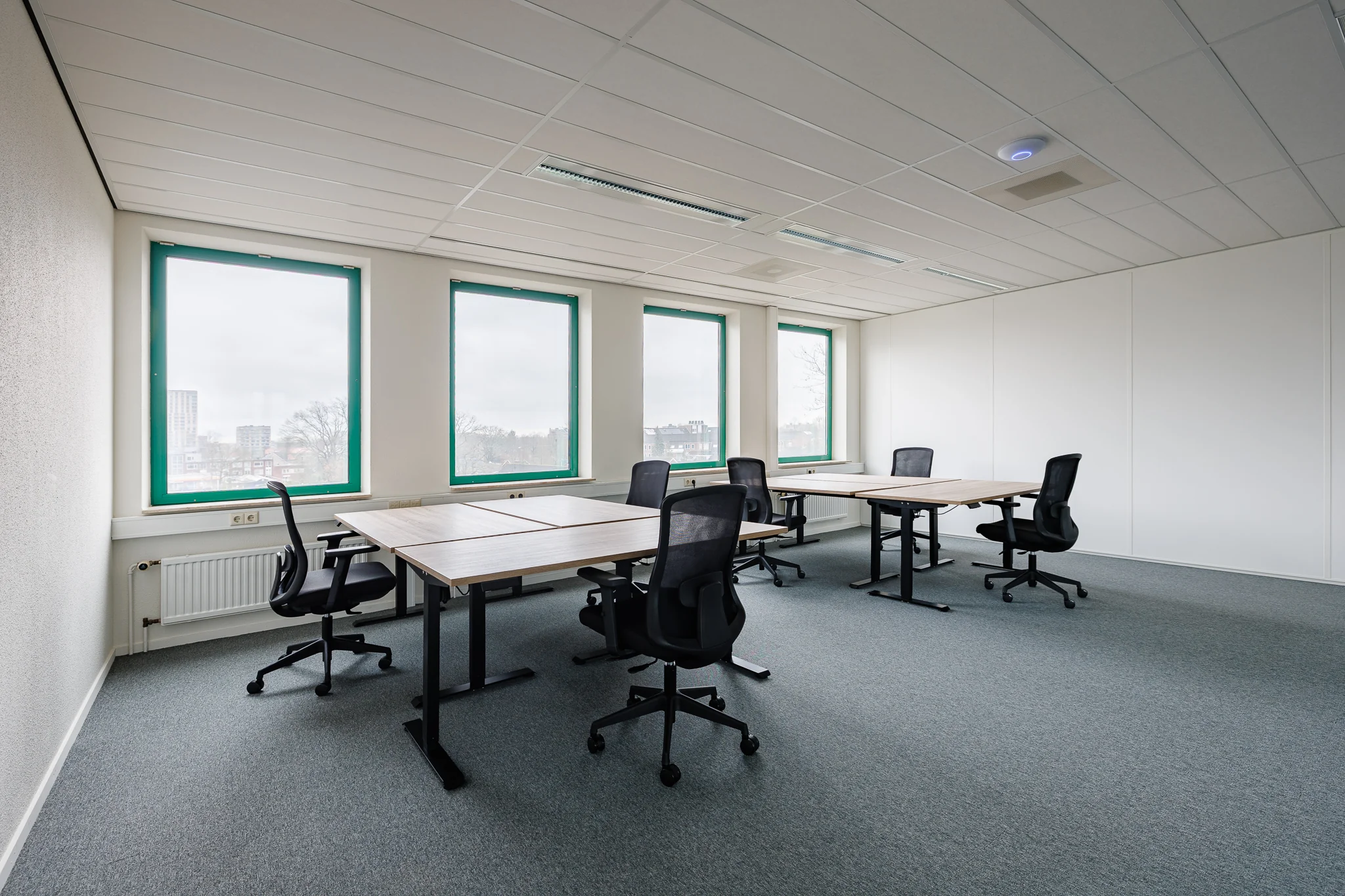 Een lege kantoorruimte met bureaus en stoelen, met uitzicht op de stad door grote ramen.