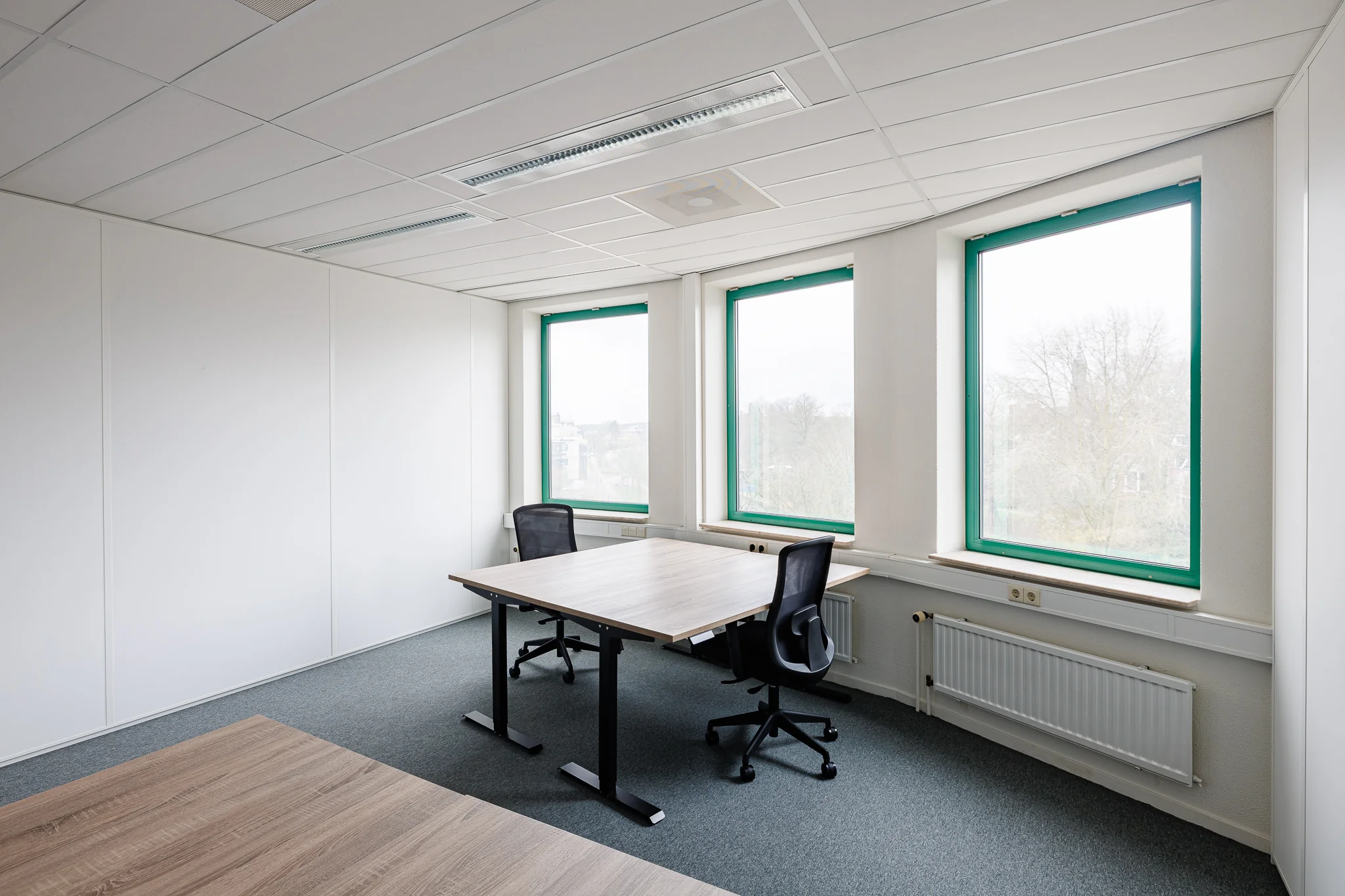 Een lichte kantoorruimte met twee bureaus en stoelen bij grote ramen in Amersfoort.