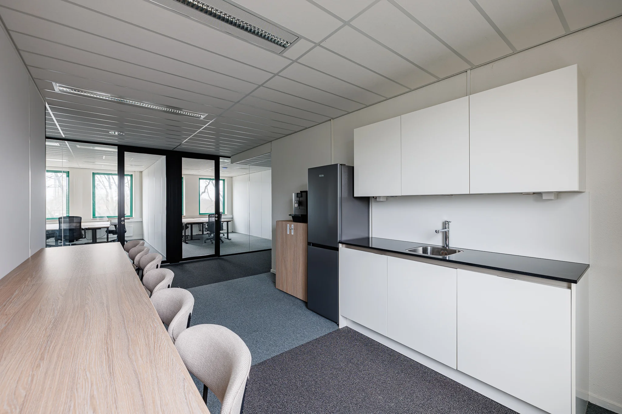 Een moderne kantoorruimte met een keukenblok, vergadertafel en glazen deuren.