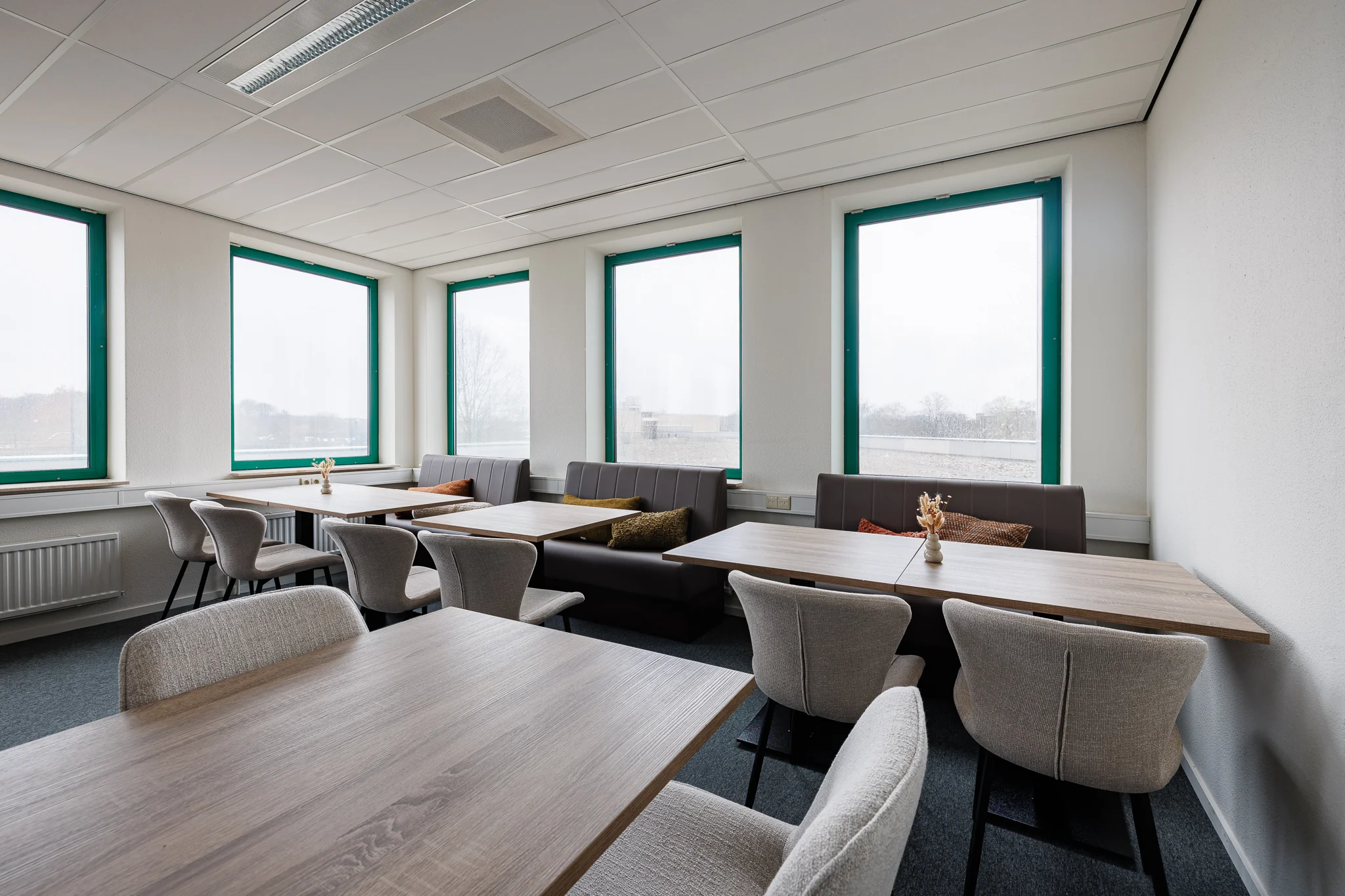 Een moderne vergaderruimte met houten tafels en gestoffeerde stoelen bij grote ramen in Stadsring 201, Amersfoort.