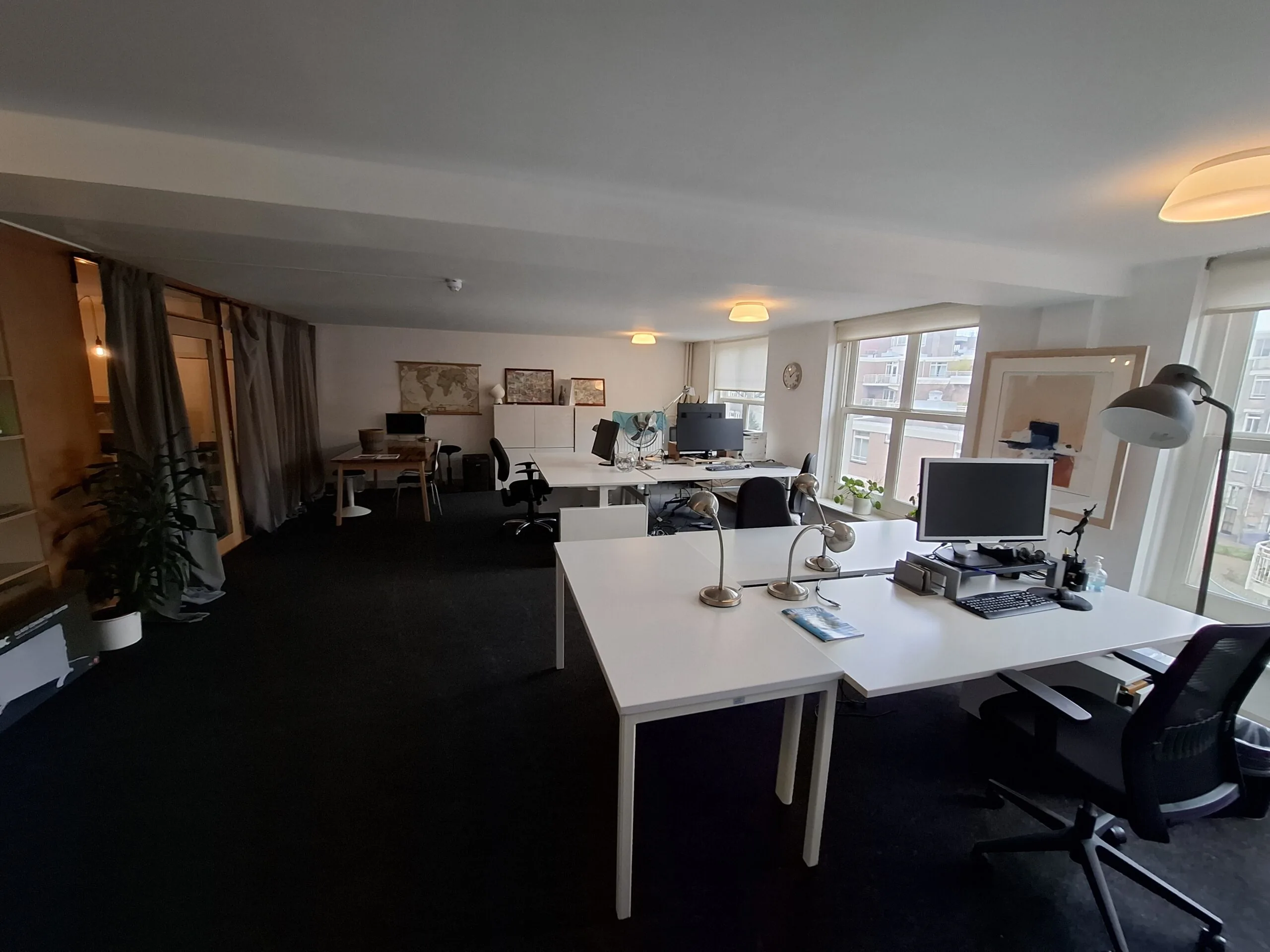 Modern en licht kantoor met meerdere werkplekken, computers en grote ramen met uitzicht op een woonwijk.