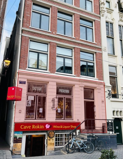 Voorgevel van een pand aan het Rokin met op de begane grond wijnwinkel Cave Rokin en erboven een tatoeage- en piercingshop.