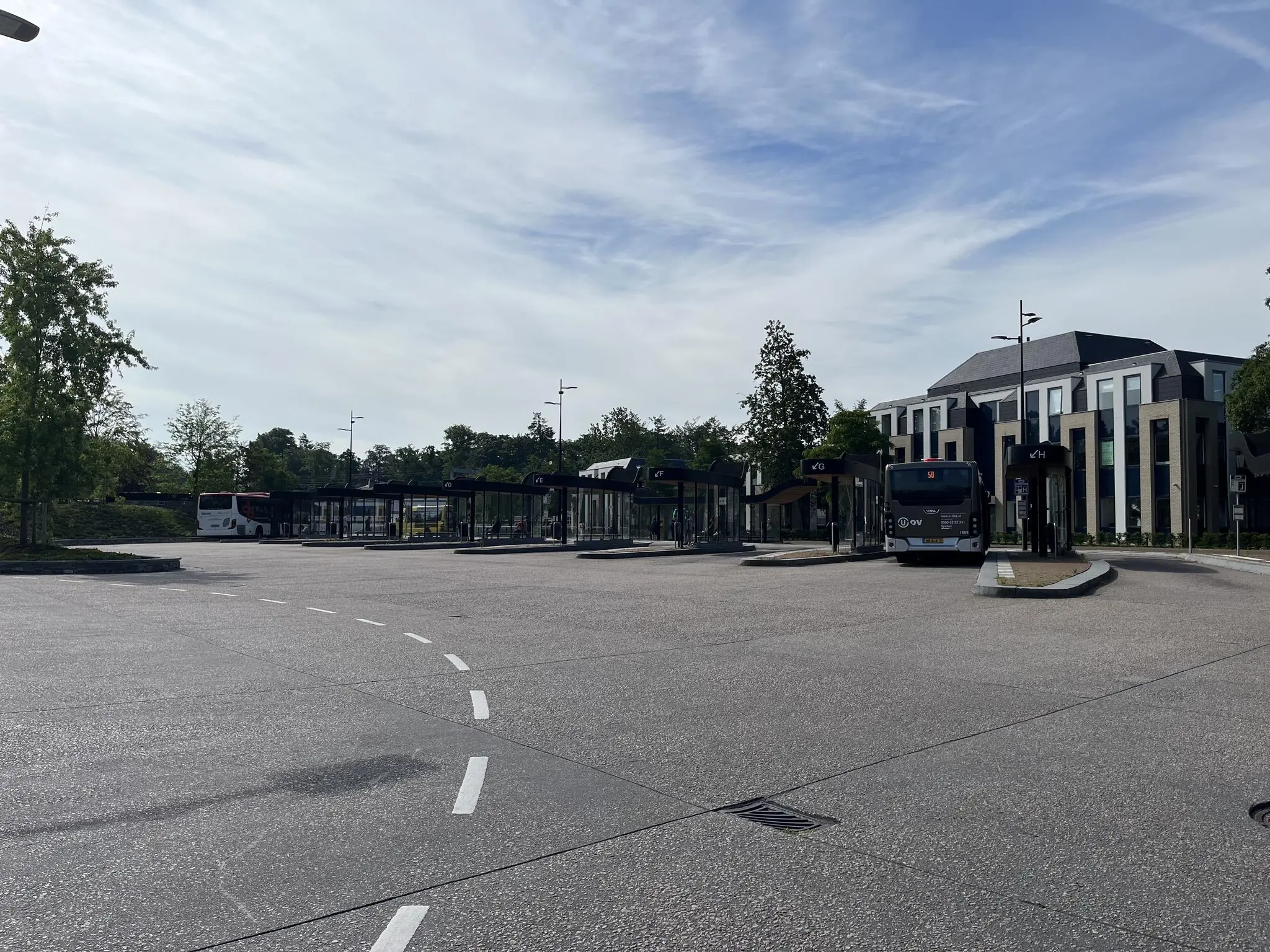 Busstation aan de Kwekerijweg met meerdere bussen en wachthokjes op een rustige ochtend.