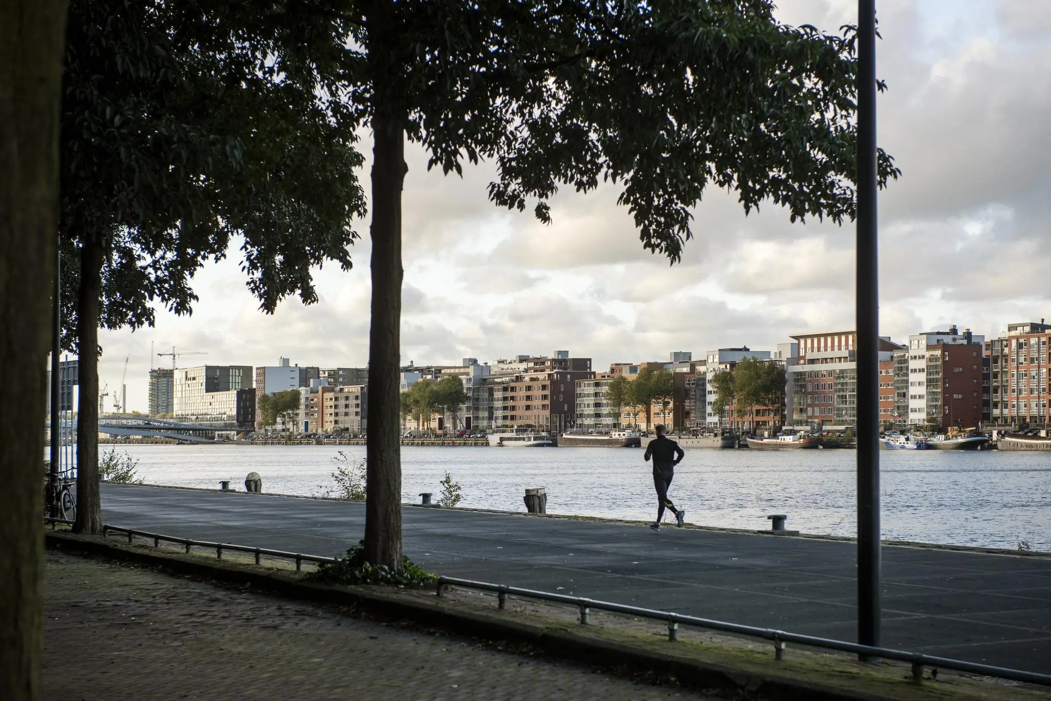 Jogger rent langs het water met uitzicht op de moderne woongebouwen van Rietlandpark in Amsterdam.