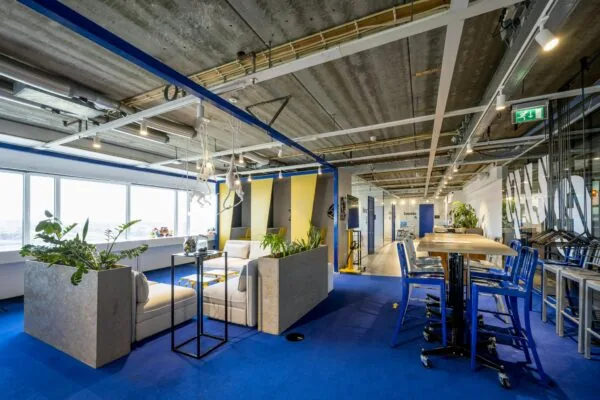 Modern kantoorinterieur aan de Johan Huizingalaan met blauwe vloer, open plafonds, zitgedeelte en werkplekken.