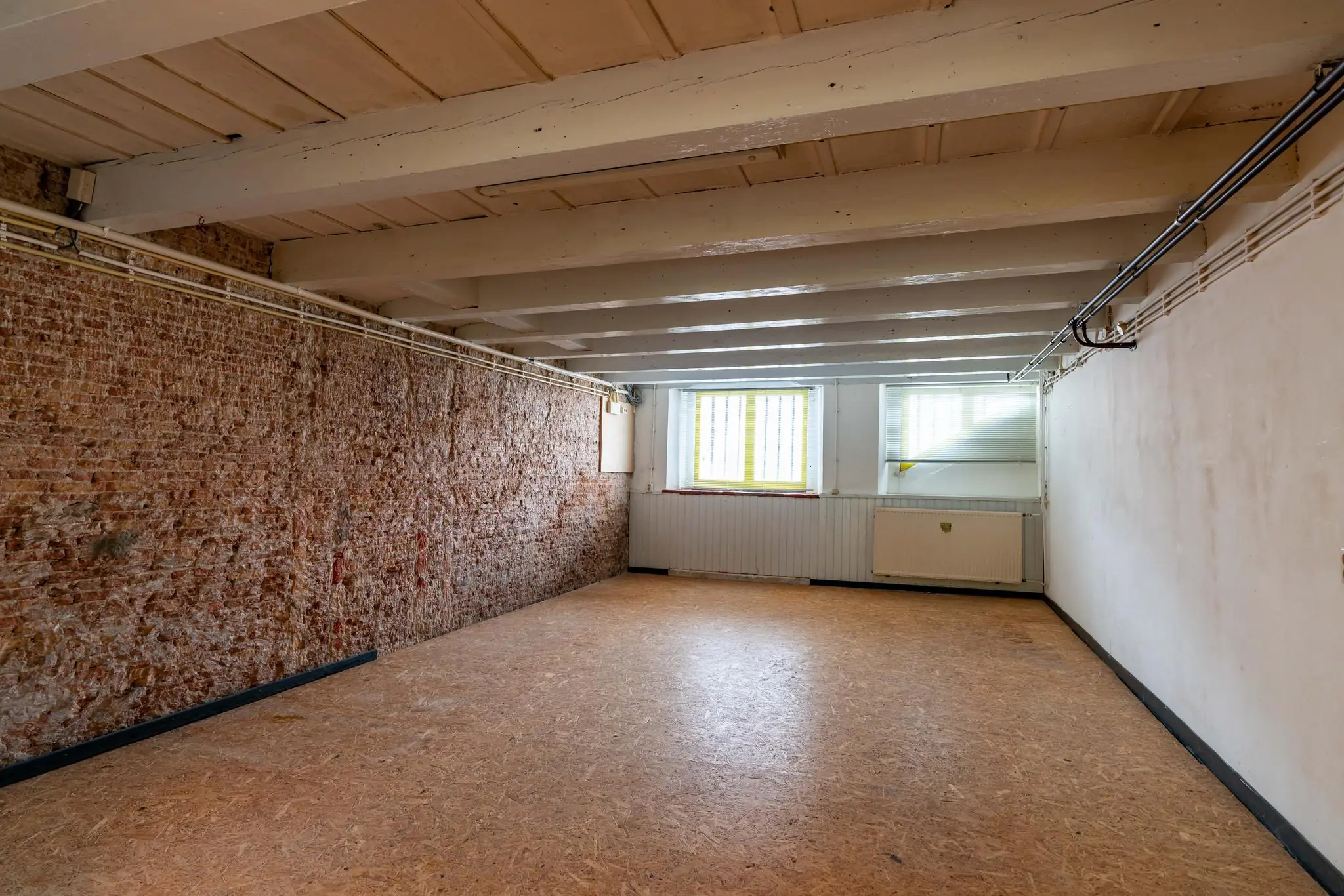 Lege souterrainruimte aan de Prinsegracht met houten plafond, bakstenen muur en twee ramen met tralies.