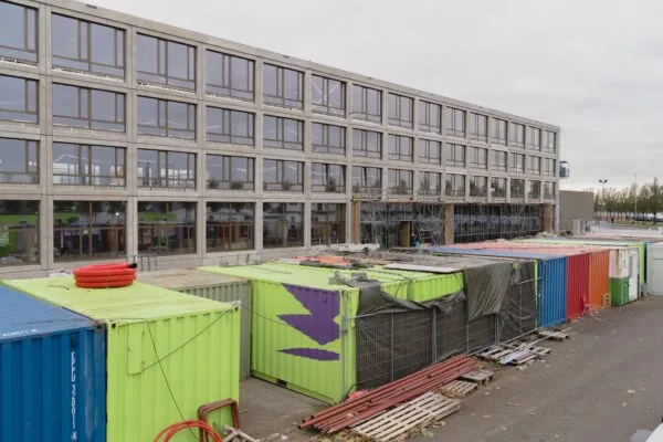 Bouwplaats aan de Sluisjesdijk met kleurrijke containers en een modern kantoorgebouw in aanbouw.