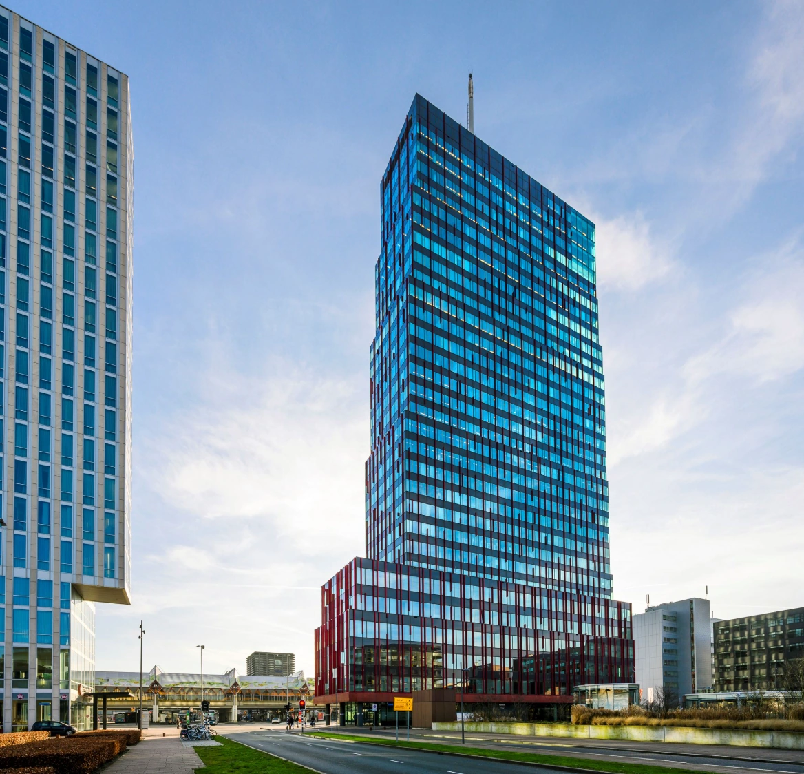Hoog modern kantoorgebouw aan de P.J. Oudweg in Almere met een glazen gevel en roodkleurige onderbouw.