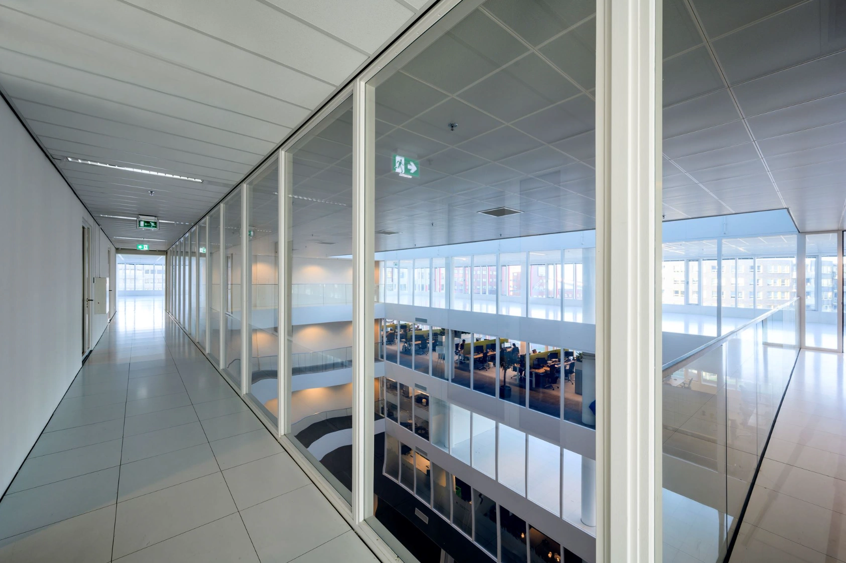 Lange glazen gang met uitzicht op meerdere etages van een modern kantoorpand aan de P.J. Oudweg.