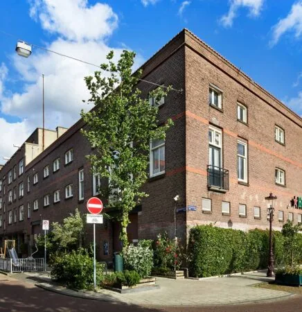 Hoekpand aan de Ruysdaelkade in Amsterdam met bakstenen gevel, balkon en groene beplanting op de stoep.