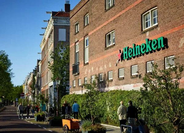 Straatbeeld van de Ruysdaelkade in Amsterdam met voorbijgangers en een Heineken-logo op een bakstenen gevel.