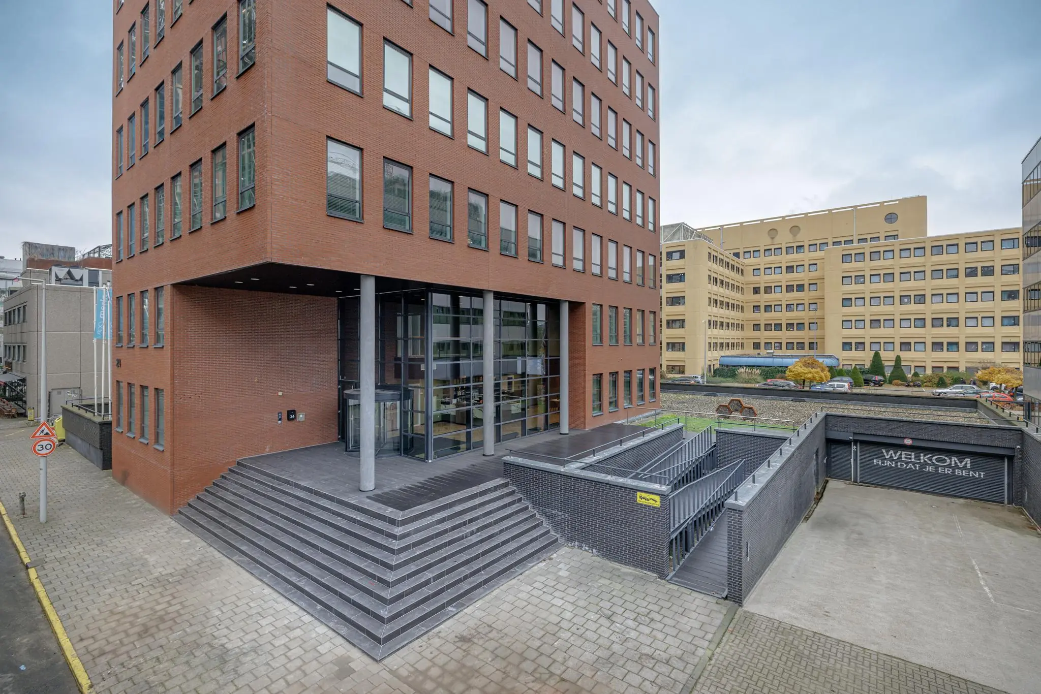 Ingang van een modern kantoorgebouw aan de Hiridostraat met brede trap, glazen entree en ondergrondse parkeergarage.