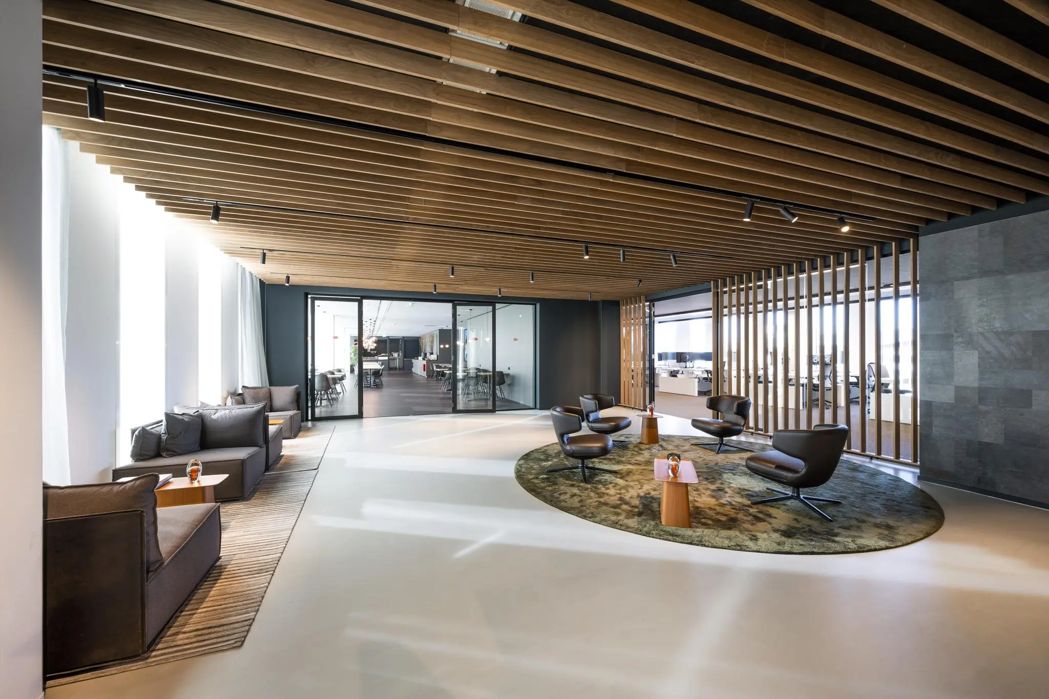 Moderne wachtruimte in kantoorgebouw Hoekenrode met loungestoelen, houten plafond en glazen vergaderruimtes.