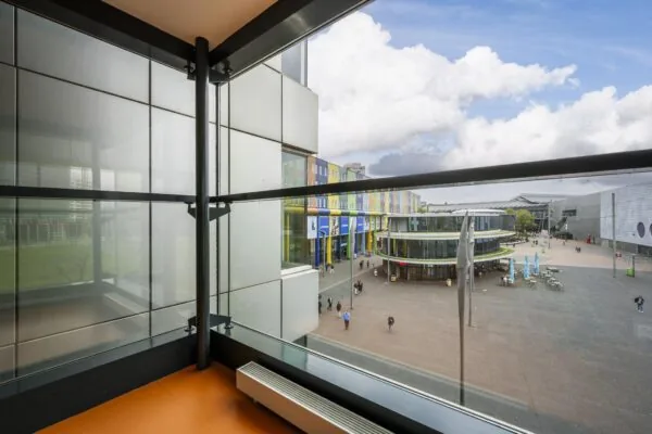 Uitzicht vanaf een balkon op de Johan Cruijff Boulevard met kleurrijke gebouwen, winkels en een modern plein.