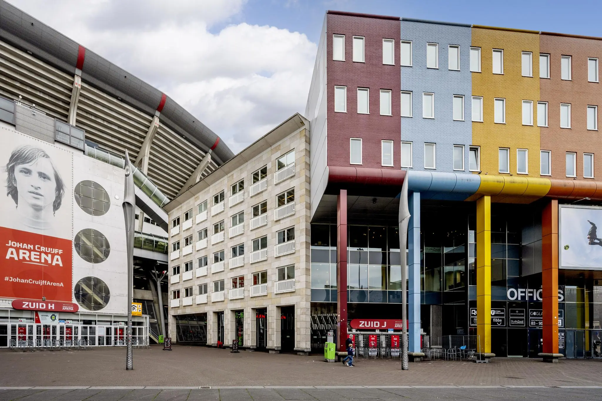 Ingang van de Johan Cruijff ArenA aan de Johan Cruijff Boulevard met kleurrijke gebouwen en een grote muurschildering van Johan Cruijff.