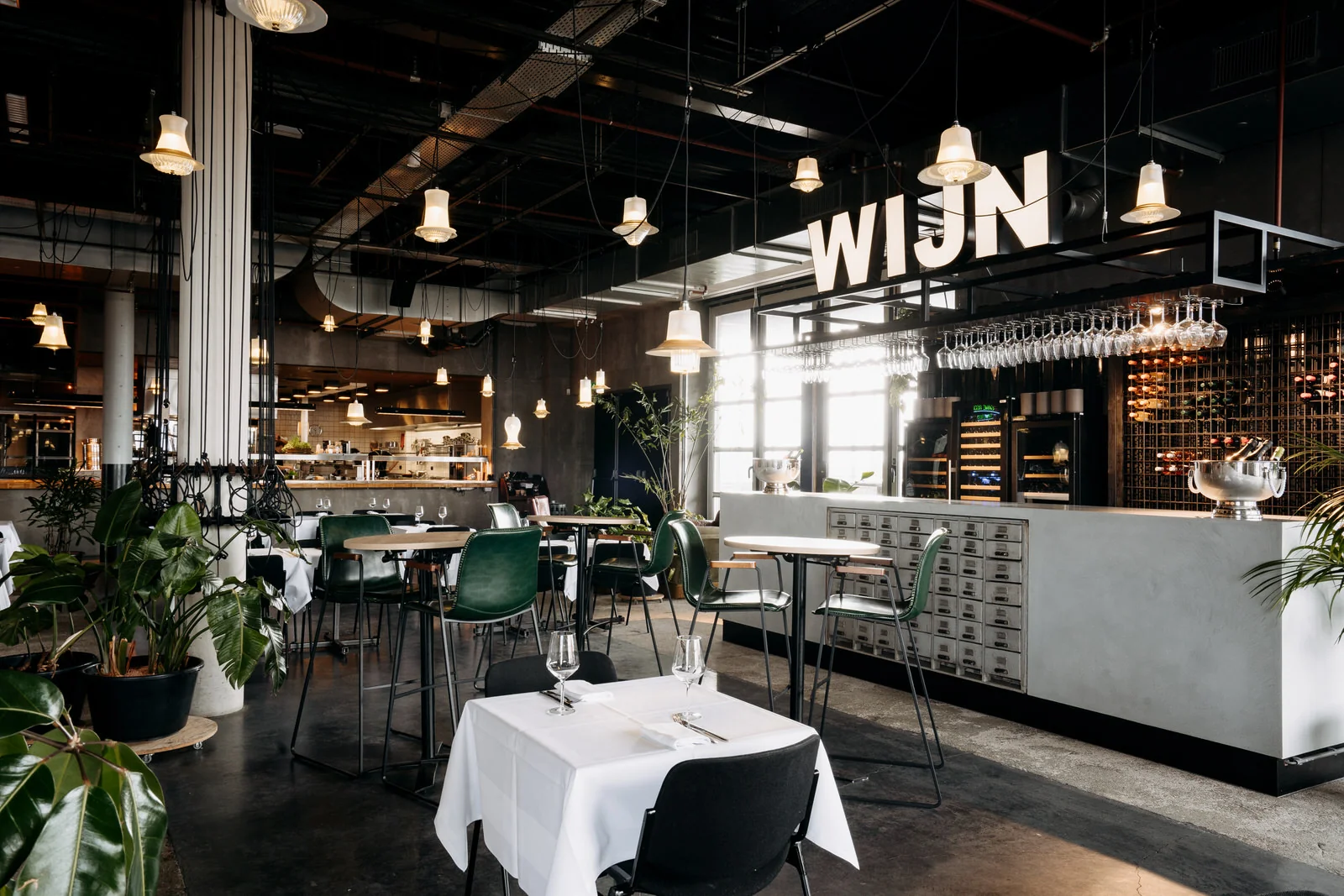 Modern restaurantinterieur aan de Johan Huizingalaan met een wijnbar, hanglampen en groen meubilair.