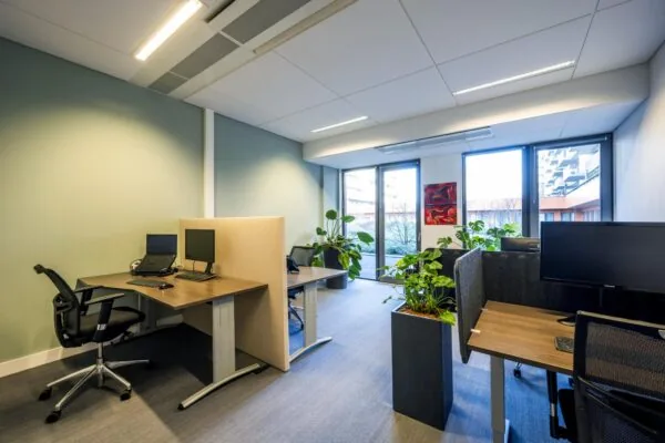 Modern kantoor met werkplekken, planten en ramen met uitzicht op de Laan van de Helende Meesters.