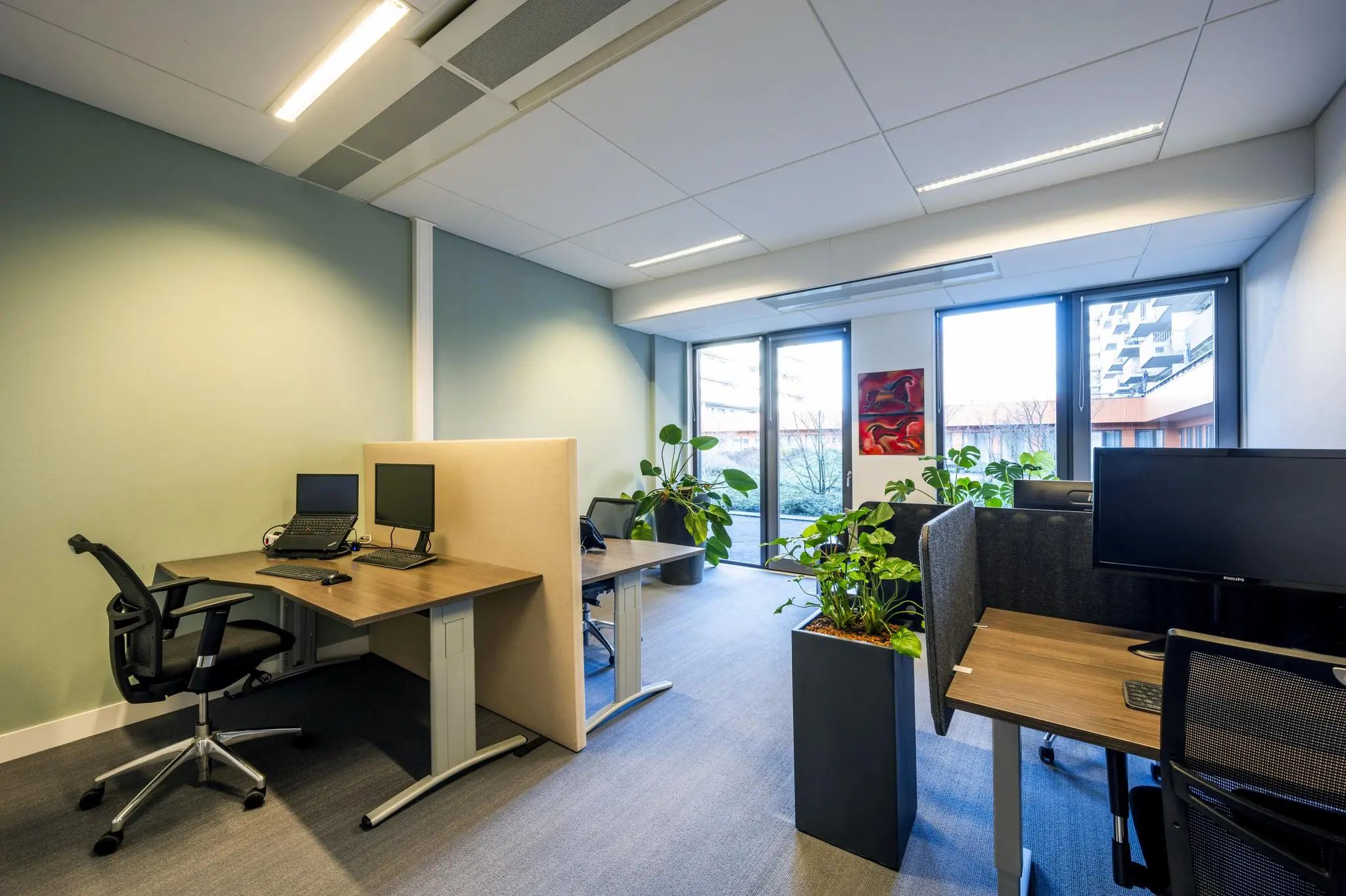 Modern kantoor met werkplekken, planten en ramen met uitzicht op de Laan van de Helende Meesters.