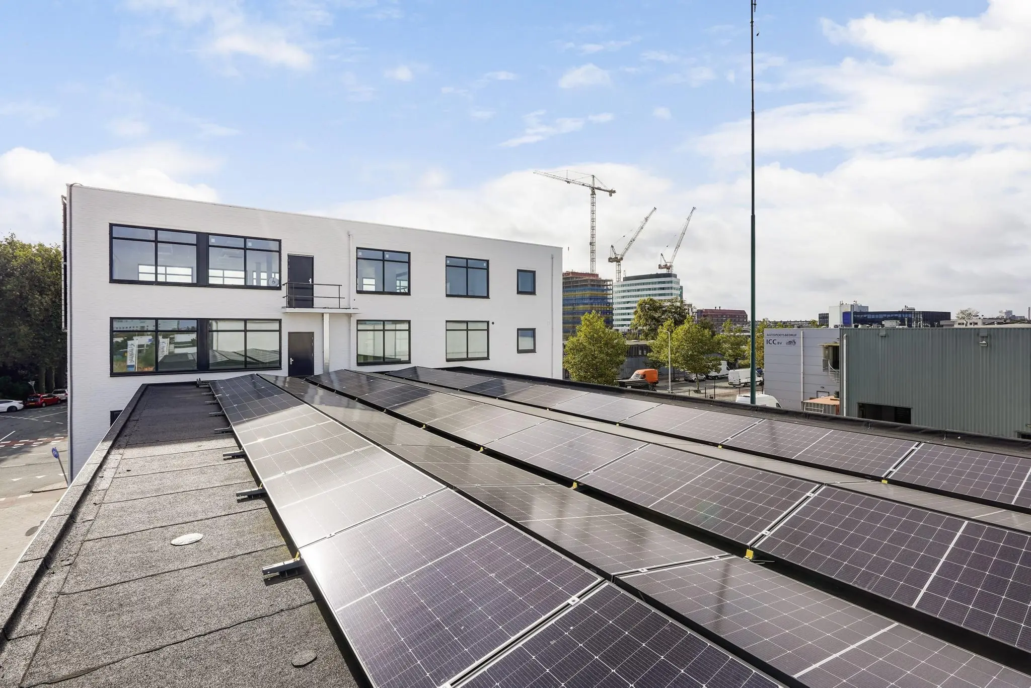 Wit bedrijfsgebouw aan de Mercuriusweg met zonnepanelen op het dak en een stedelijk uitzicht met hijskranen op de achtergrond.