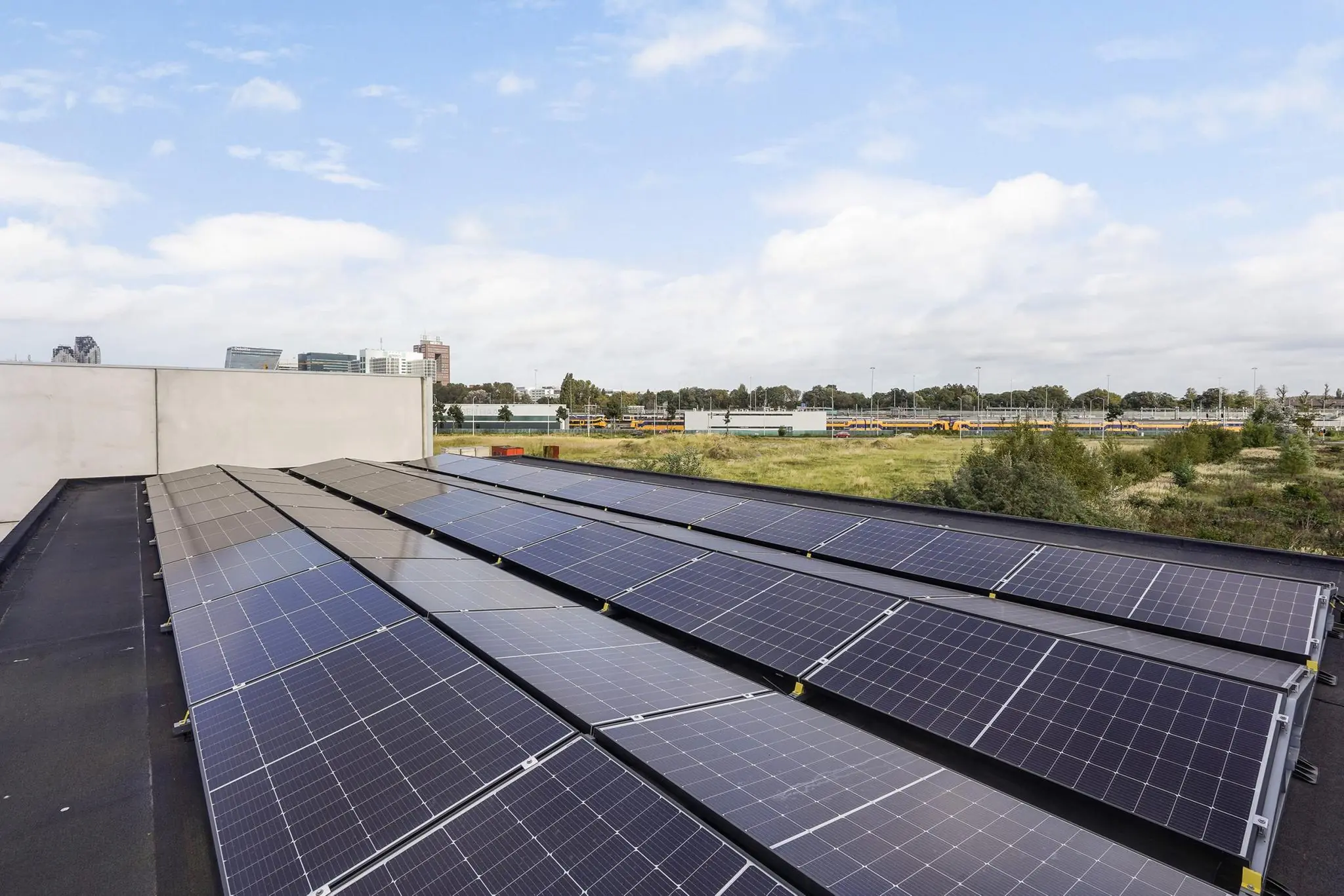 Zonnepanelen op het dak van een gebouw aan de Mercuriusweg met uitzicht op een groen terrein en kantoren op de achtergrond.