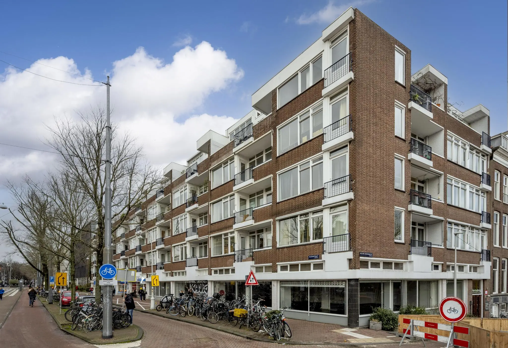 Hoekpand aan de Muiderstraat in Amsterdam met meerdere woonlagen, balkons en geparkeerde fietsen langs de stoep.