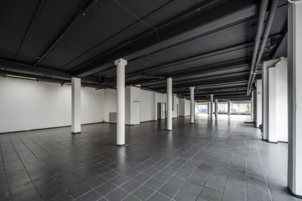 Leeg bedrijfspand aan de Muiderstraat met zwarte tegelvloer, witte pilaren en grote ramen aan de straatzijde.
