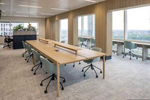 Modern kantoorinterieur op Amstelplein met houten werktafels, bureaustoelen en uitzicht op de stad.