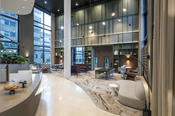 Moderne en stijlvolle lobby van een kantoorgebouw aan het Amstelplein, met hoge plafonds, grote ramen en diverse zitgelegenheden.