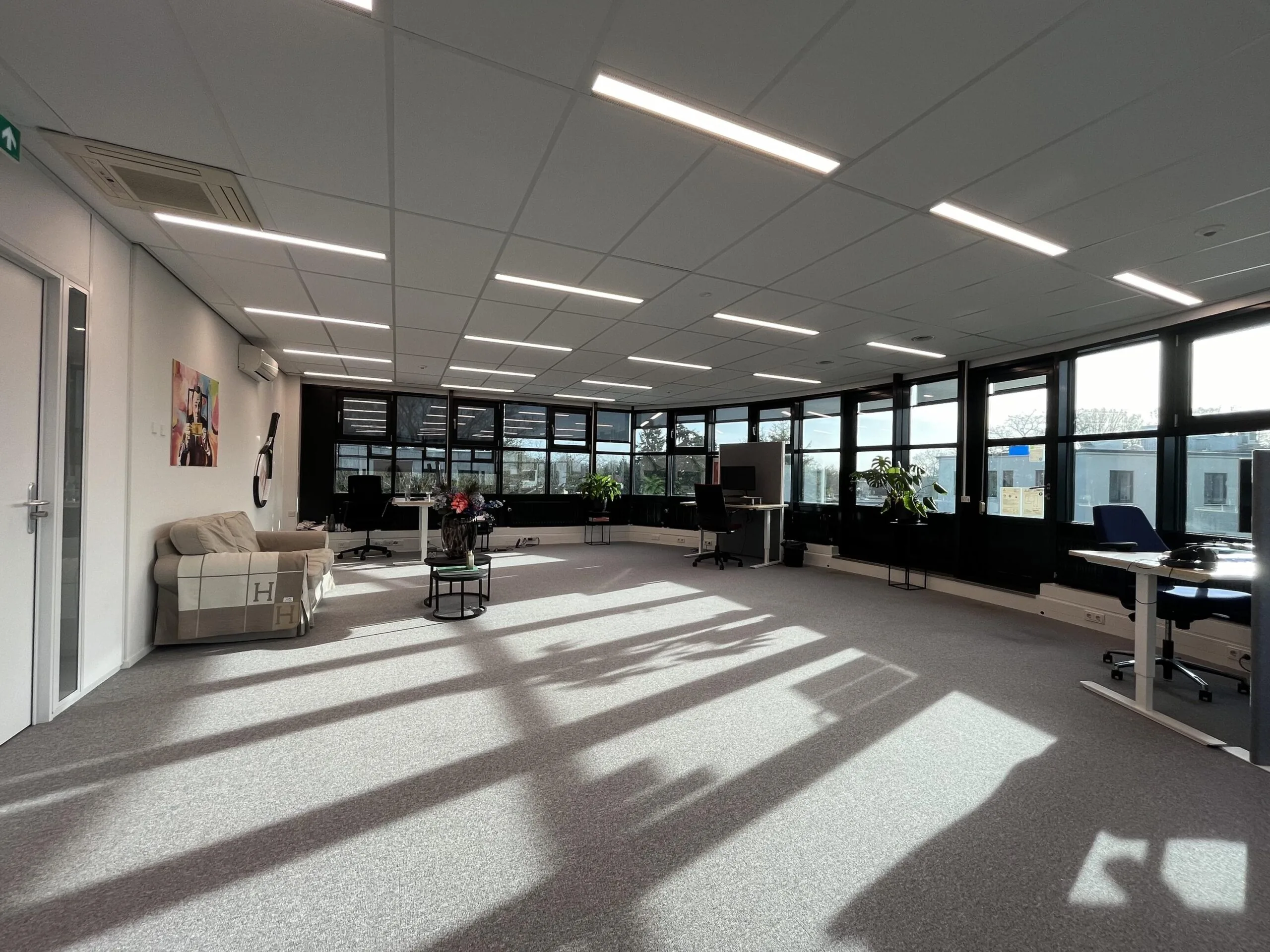 Een modern en ruim kantoor met veel natuurlijk lichtinval door grote ramen.