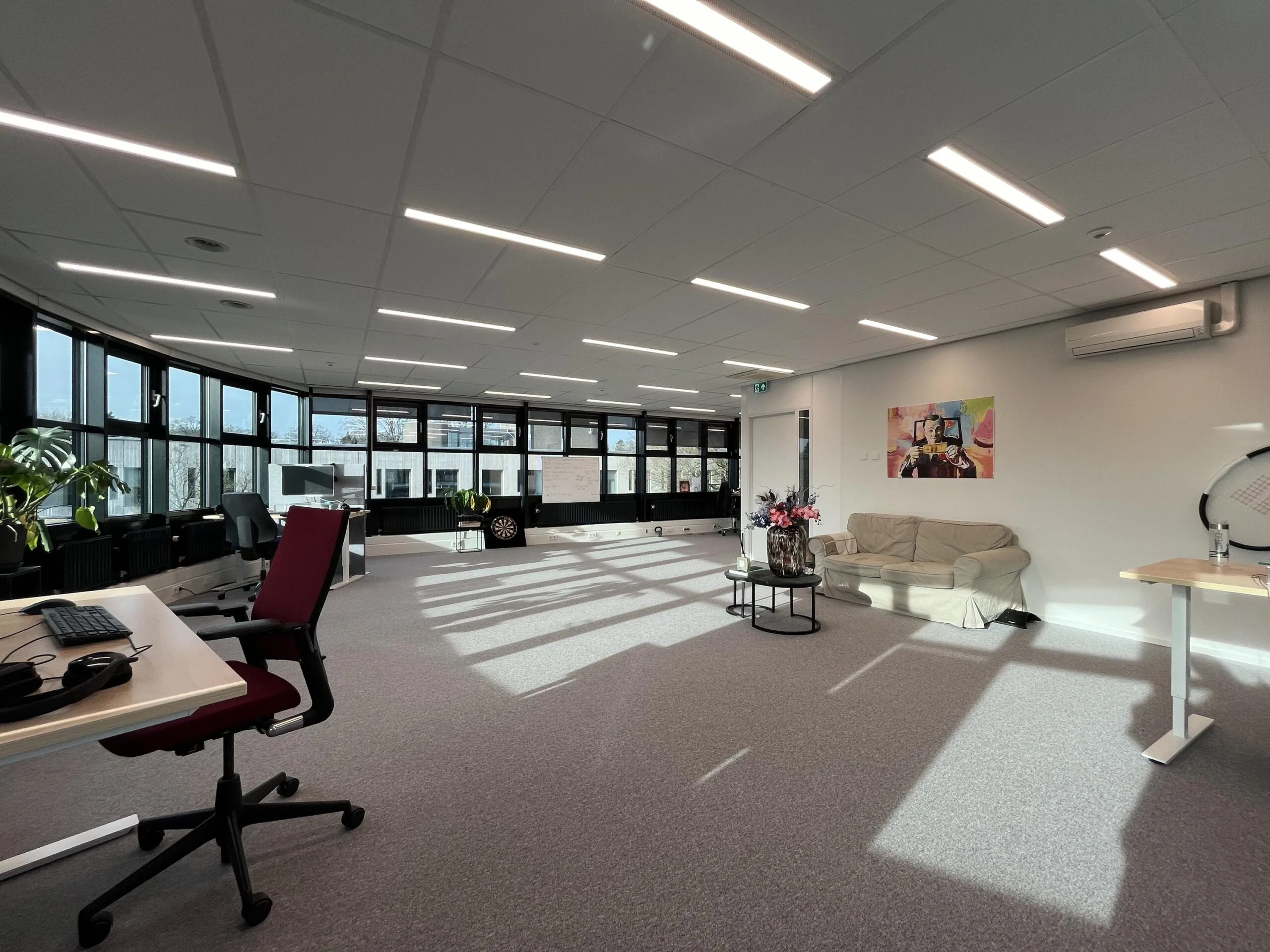 Een ruim, modern kantoor met veel natuurlijk licht, zitbanken en bureaus.