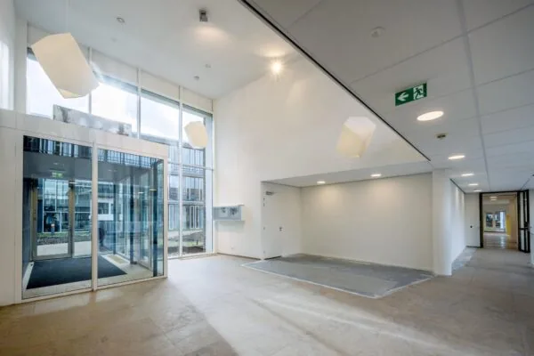 Moderne, lichte entreehal van een gebouw aan de De Cuserstraat met grote ramen en geometrische hanglampen.