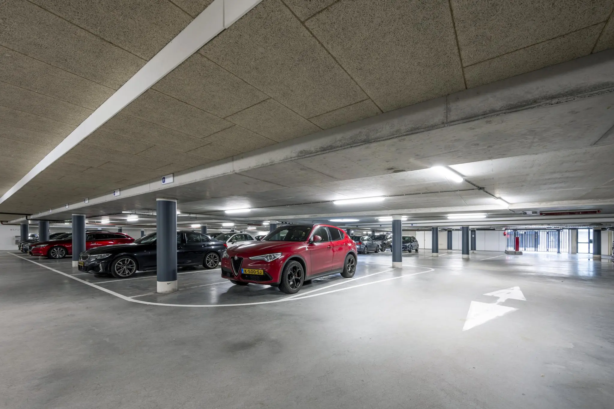 Ondergrondse parkeergarage aan de De Cuserstraat met meerdere geparkeerde auto’s, waaronder een rode SUV op de voorgrond.
