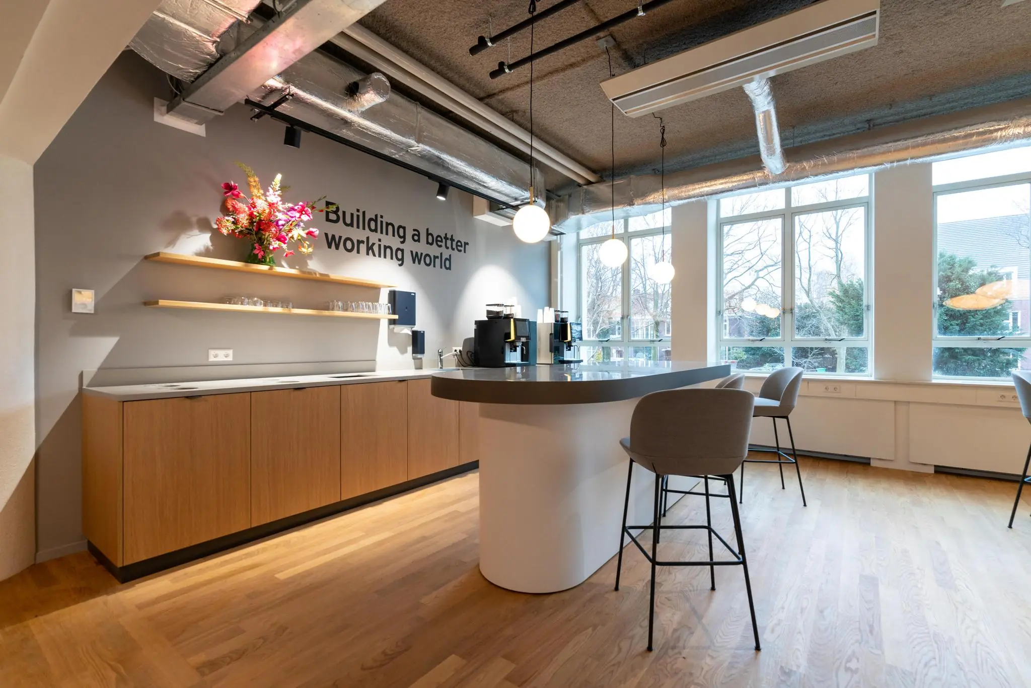 Moderne kantoorkeuken aan de Wassenaarseweg met een koffiecorner, zitgedeelte en de tekst "Building a better working world" op de muur.