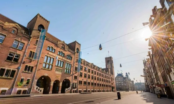 Zonnige straat op het Damrak in Amsterdam met de Beurs van Berlage prominent in beeld.