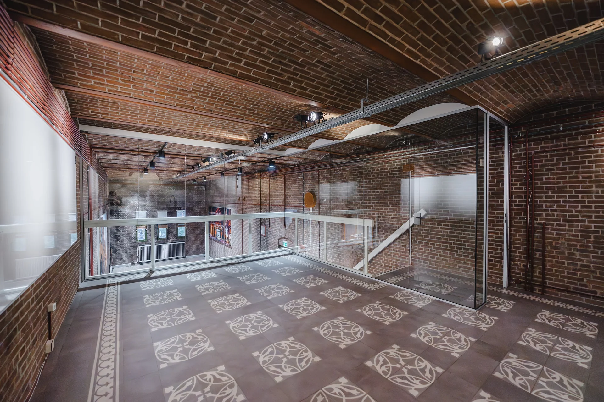 Binnenterras met glazen balustrade en decoratieve tegelvloer in een modern gerenoveerd bakstenen gebouw aan het Damrak.