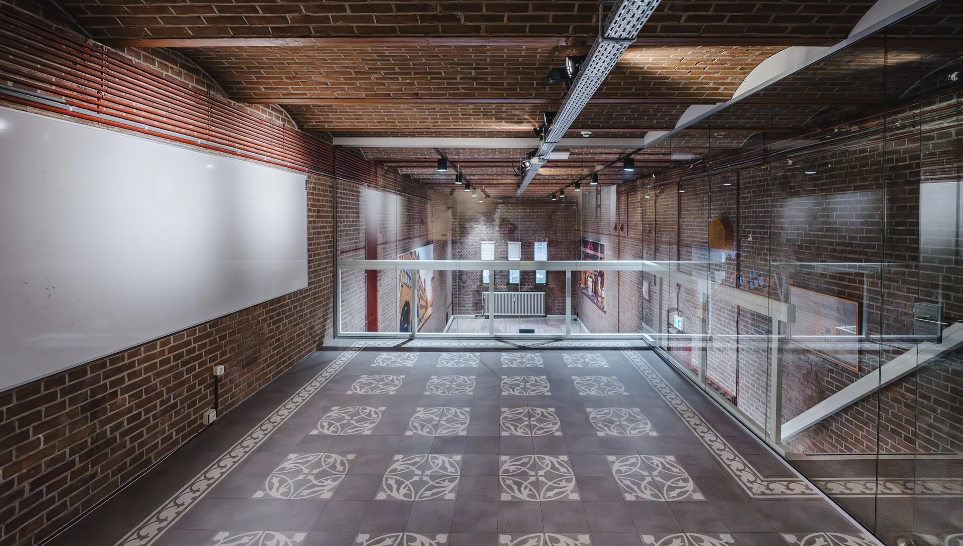 Modern interieur van een gang met bakstenen muren, glazen wanden en een betegelde vloer met siermotief in gebouw aan het Damrak.