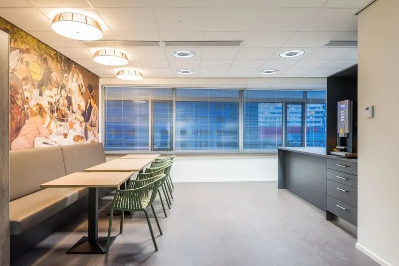 Moderne bedrijfskantine met strakke meubels, een grote muurschildering en een koffieautomaat in de hoek.