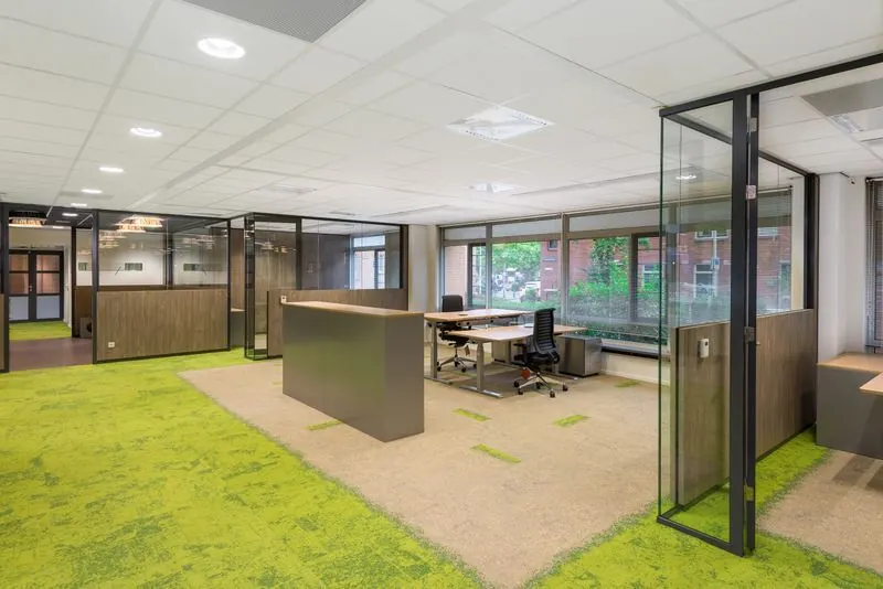 Moderne kantoorruimte aan het Spui met glazen wanden, open werkplekken en groen-beige tapijt.