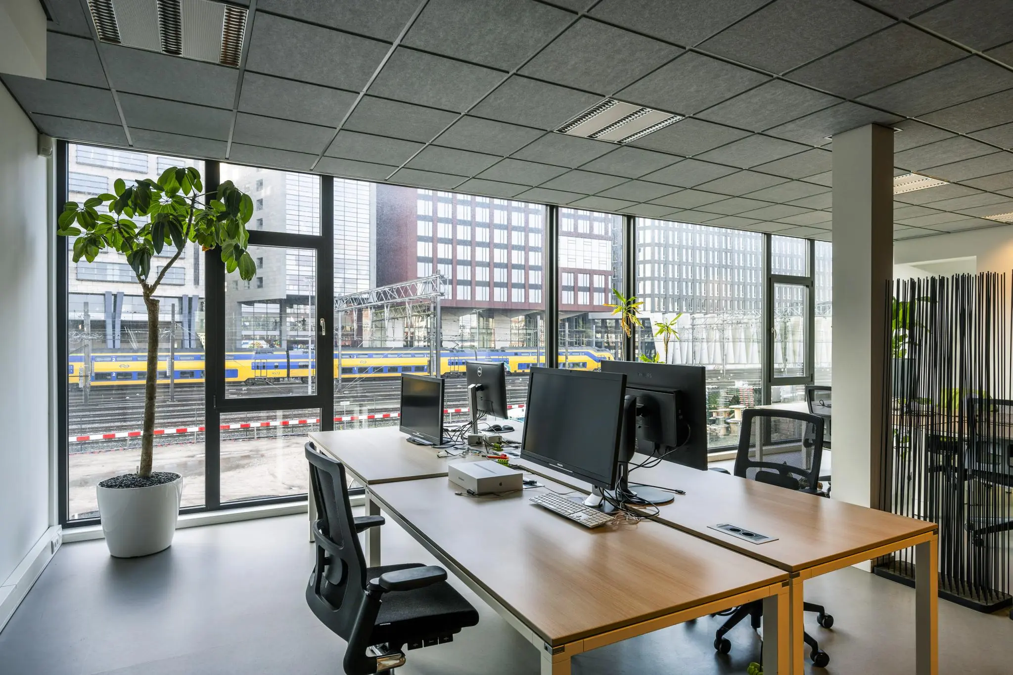Modern kantoorinterieur met uitzicht op spoorlijn en gebouwen aan de De Ruijterkade in Amsterdam.